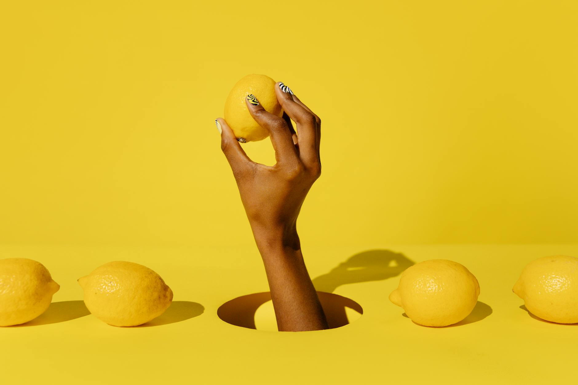 A hand holds a fresh lemon against a vivid yellow background