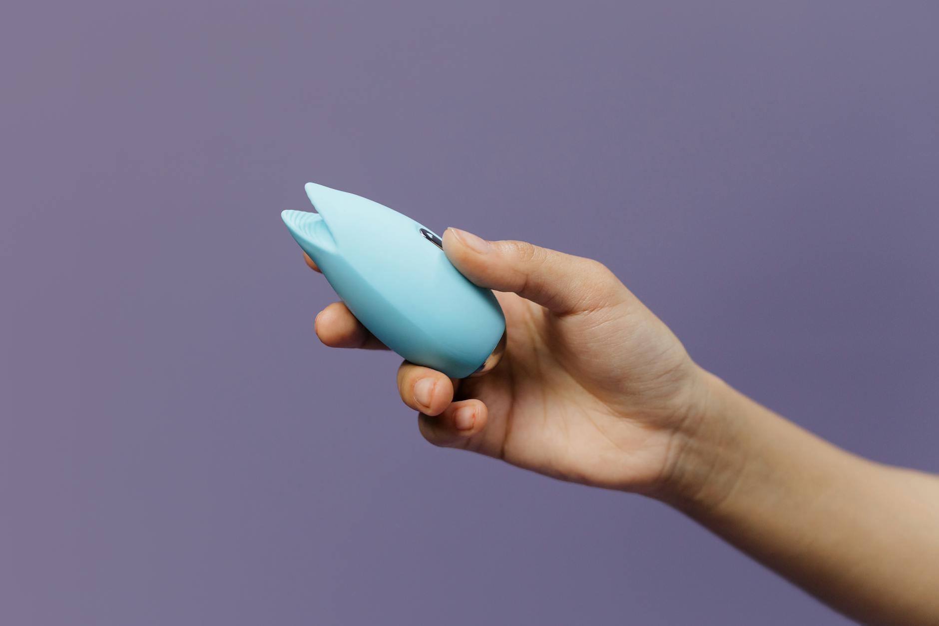 A blue silicone lemon clitoral vibrator held in hand against a soft purple background